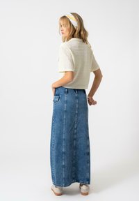 Haut blanc texturé à manches courtes associé à une longue jupe en denim bleu clair avec des coutures latérales et des poches, portée avec des baskets neutres.