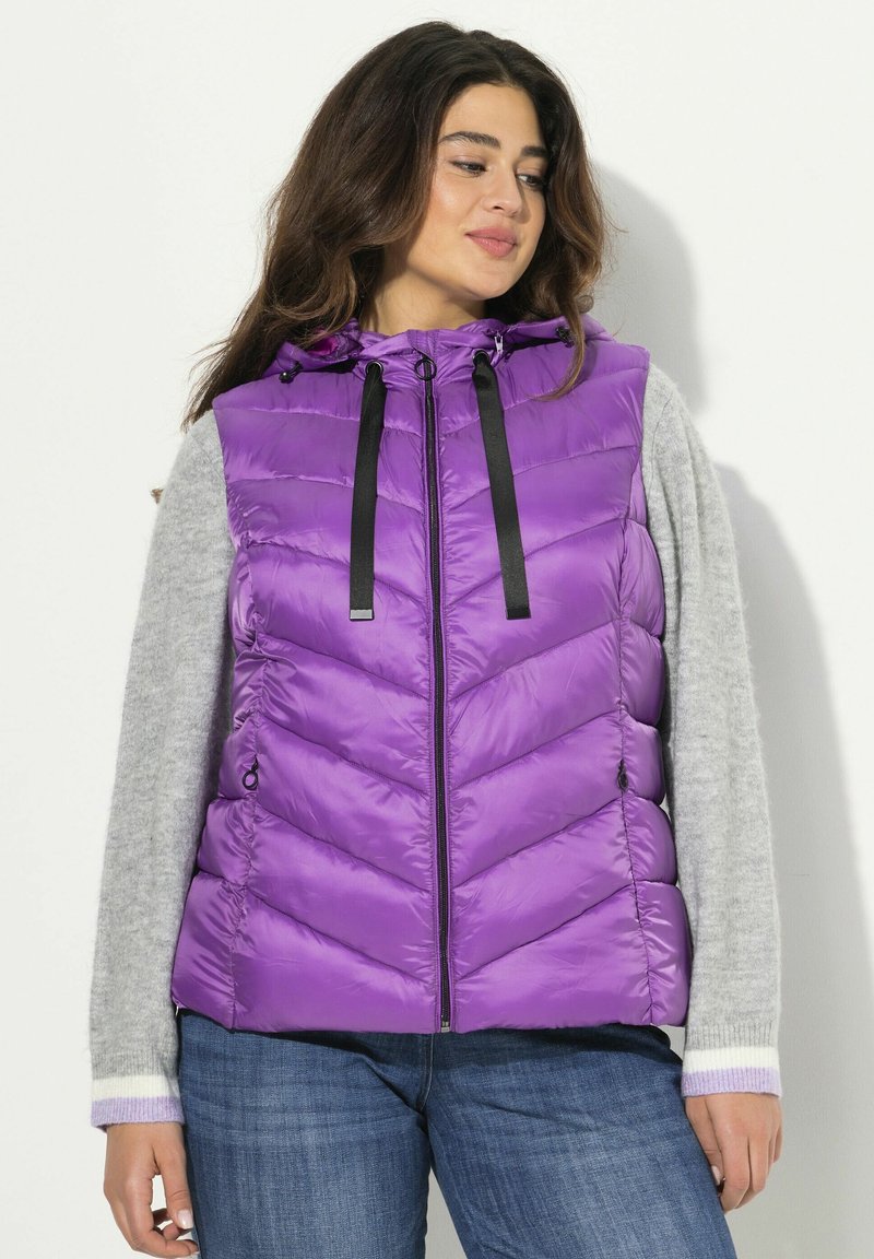 Gilet imbottito viola con cappuccio, dotato di zip nera e cordini. Motivo a chevron, abbinato a una maglietta a maniche lunghe grigia.