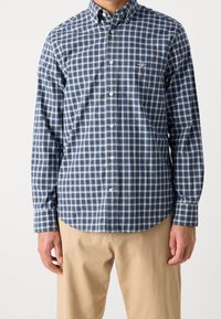 Koszula na guziki w niebiesko-białą kratę, z klasycznym kołnierzem, długimi rękawami i subtelnym logo marki na piersi. Tkanina odporna na zagniecenia.