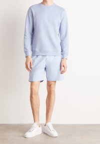 Felpa azzurra con collo a giro e pantaloni corti azzurri abbinati. Sneakers bianche completano il look. Tessuto morbido, design casual.