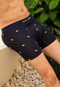 Černé boxerky s malými oranžovými vzory ovoce, měkká látka, elastický pás s nápisem "HAPPY SHORTS" v oranžové barvě.
