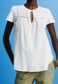 Top bianco a maniche corte con strisce testurizzate e dettagli ricamati. Presenta un collo a fessura con un laccetto e una vestibilità rilassata.