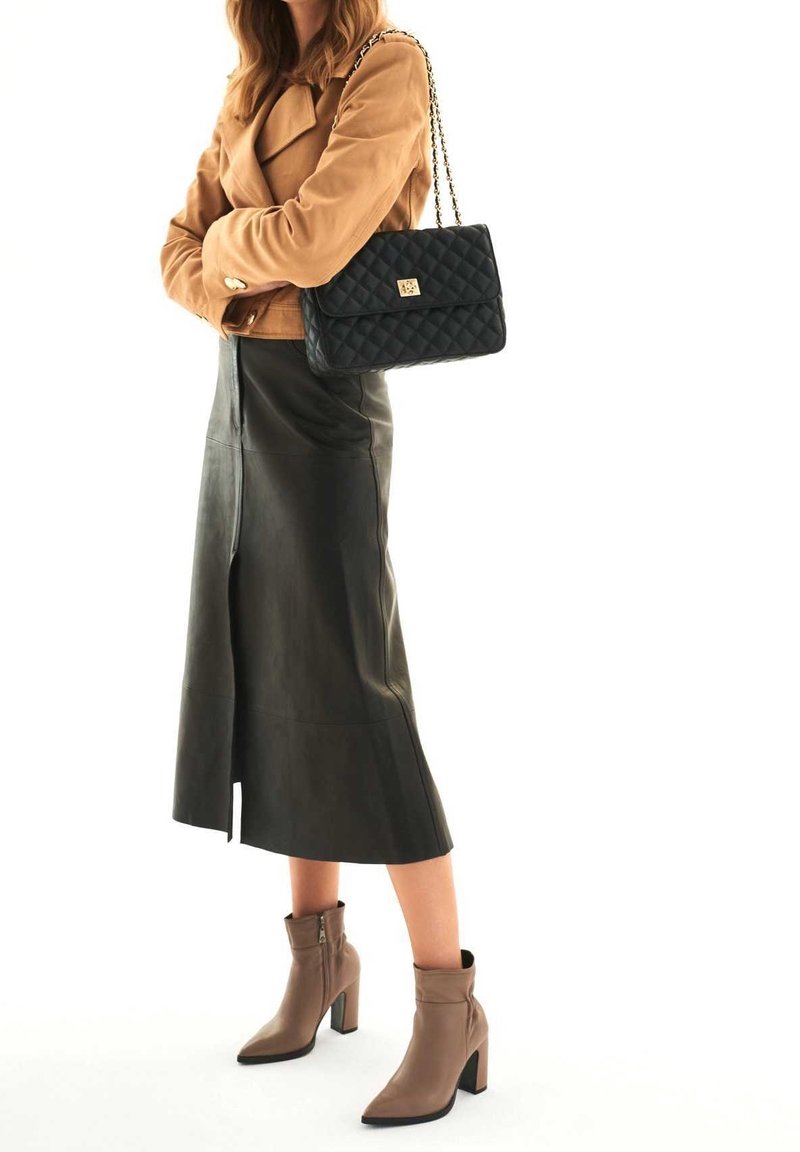 Giacca scamosciata sabbia, borsa nera trapuntata con chiusura dorata, gonna midi in pelle nera e stivaletti taupe con punta affilata e tacco a blocco.