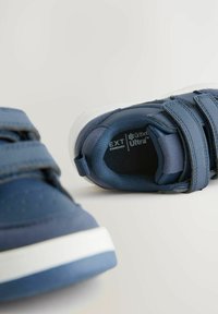 Niebieskie buty sportowe o gładkiej fakturze, z rzepami i białymi środkami. Posiadają logo wewnątrz buta oraz elegancki, nowoczesny design.
