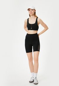 Mustat urheilu crop top, jossa on etupainikkeet, ja yhteensopivat korkeat pyöräilyshortsit, joissa on verkkokankaiset sivupaneelit ja urheilujalkineet.