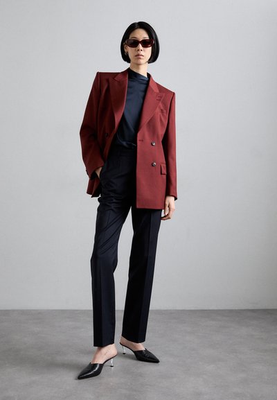 Burgundy double-breasted blazer over a navy top, paired with tailored black trousers and black mules featuring a metallic heel.