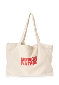 Sac en toile crème avec le texte "AMERICAN VINTAGE" en rouge gras. Doté de longues anses solides et d'une surface douce et texturée.
