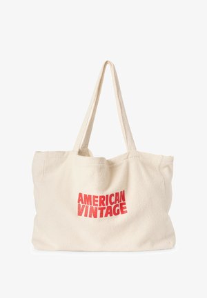 Kremkrāsas kanvas maisiņš ar tekstu "AMERICAN VINTAGE" biezs sarkanā krāsā. Tam ir gari, izturīgi rokturi un maiga, teksturēta virsma.