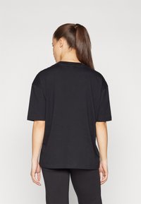 Svart oversized t-skjorte med rund hals, korte ermer og rett snitt, laget av myk stoff. Bæres med sorte leggings.