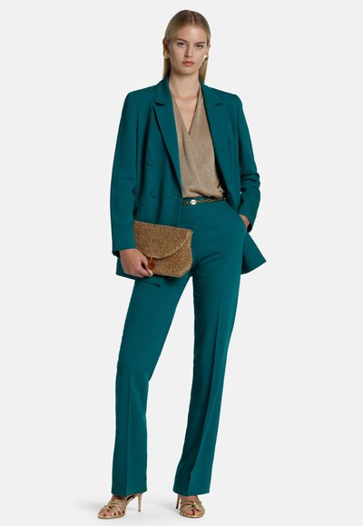 Teal tailored suit with a textured fabric, paired with a gold shimmer top. Accessories include a gold belt and a woven clutch.