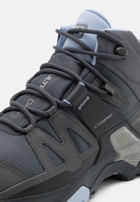 Chaussure de sport grise avec une tige texturée en matières synthétiques et en maille, maintenue par des lacets gris, et avec un col rembourré bleu clair.