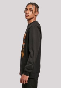 Melna kapucīna džemperis, izgatavots no kokvilnas materiāla, priekšā ar krāsainiem grafiskiem zīmējumiem ar multfilmu tēliem, ar ribotiem piedurknēm un apakšmalu.