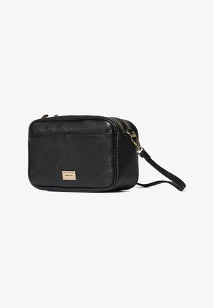 Pochette bracelet en cuir texturé noir avec fermeture éclair dorée et plaque frontale rectangulaire, bandoulière détachable sur fond blanc.