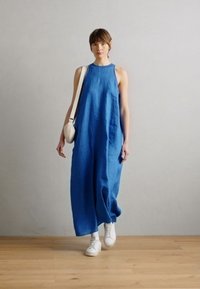 Lång, ärmlös klänning i blått linnetyg med en loose fit, rund halsringning och sidfickor, ihop med vita sneakers.