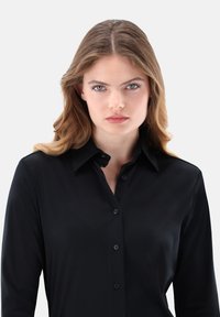 Black button-up shirt with a collar, long sleeves, soft texture, and a fitted design. Features front buttons and a smooth finish.
