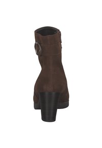 Brown suede ankle boot with a rounded toe, a side zipper, and a decorative strap featuring a circular accent. Chunky heel.