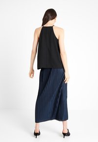 Canotta nera senza maniche abbinata a una lunga gonna blu navy plissettata. L'outfit presenta una vestibilità comoda e un tessuto morbido, creando una silhouette fluida.