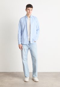 Lichtblauw overhemd met knopen, gecombineerd met een crèmekleurige trui, lichte denim jeans en witte sneakers. Eenvoudig ontwerp en relaxte pasvorm.