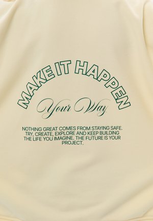 Tekst op beige stof: "LAAT HET GEBEUREN Op jouw manier. Niets groots komt voort uit veilig blijven. Probeer, creëer, ontdek en blijf het leven bouwen dat je voorstelt."