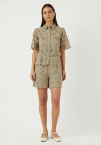 Lys beige to-delt sett som består av en kortermet, kragebelagt skjorte med knapper og matchende shorts, laget av blonder med blomstermønstre og bølgete kanter.