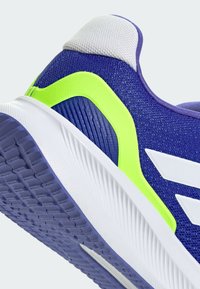La chaussure de sport violette dispose d'un dessus en maille respirante, d'une semelle intermédiaire blanche et de accents vert fluo, avec une semelle extérieure en caoutchouc texturé pour une bonne adhérence.