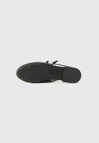 Black shoe featuring a smooth leather upper, low heel, and a textured rubber sole with ridges for grip. Two adjustable straps included.