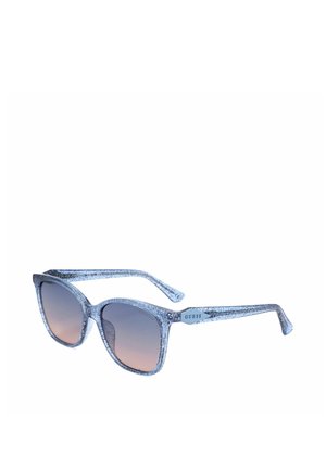Occhiali da sole con montatura in plastica trasparente blu glitterata, lenti marroni sfumate e logo Guess sulla stanghetta.