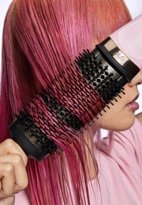 Okrągła szczotka o czarno-kolczastej nawierzchni; uchwyt jest czarny. Włosy są intensywnie różowe, proste i błyszczące, co ukazuje szczotkę w użyciu.