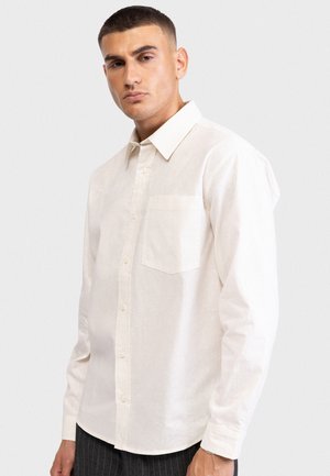 Λευκό πουκάμισο με μακριά μανίκια από ελαφρύ ύφασμα. Διαθέτει κουμπιά στο εμπρόσθιο μέρος, τσέπη στο στήθος και κλασικό γιακά.