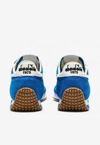 Sneakers in camoscio blu con dettagli bianchi, dotati di una suola in gomma testurizzata e logo sul tallone. Design retrò classico con una costruzione robusta.