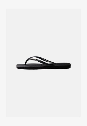 Infradito in gomma nera con suola testurizzata e sottili cinturini a forma di Y, vista laterale su sfondo neutro.