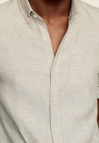 Chemise beige clair à manches courtes avec boutons, fabriquée en tissu texturé, dotée d'une poche poitrine et d'un col pointu.