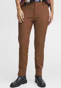 Hnědé kalhoty na míru s elegantním designem, vyrobené z hladké látky, se slim fit střihem a doplněné černými kotníkovými botami.