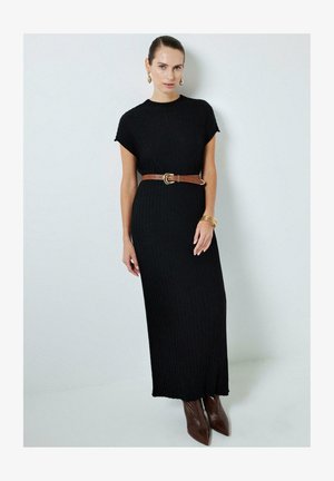 Vestido negro de punto acanalado con mangas cortas, cintura ajustada acentuada por un cinturón marrón, combinado con botas de tacón marrón con punta.