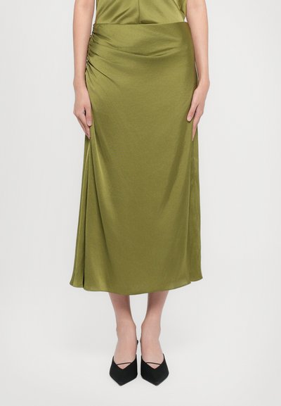 Jupe olive, longueur genoux avec un design froncé sur le côté, fabriquée en tissu lisse. Associée à des escarpins noirs à bout pointu.
