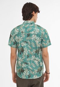 Camisa de manga corta en color aguamarina con un estampado de hojas, que presenta un cuello con botones y un dobladillo curvado. Tejido suave con un acabado texturizado.