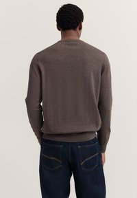Brauner Pullover aus weichem Strickstoff, mit Rundhalsausschnitt, gerippten Bündchen und Saum, kombiniert mit dunkelblauen Jeans. Rückansicht gezeigt.
