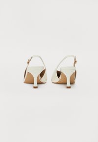 Sandales à talons en cuir verni blanc avec une bride arrière, un bout pointu et un petit talon aiguille, dotées d'une semelle en caoutchouc beige.