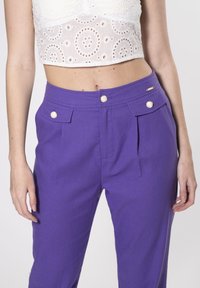 Paarse op maat gemaakte broek met voorplooien, twee zijzakken en decoratieve knopen in goudkleur. Glad textuur van de stof met een gestructureerde pasvorm.