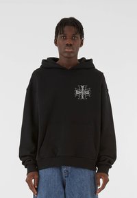 Black hooded sweatshirt with a front pocket, featuring a silver graphic design on the left chest. Made from soft, textured fabric.