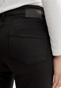 Jeans neri in denim con una tasca posteriore cucita e un'etichetta in pelle con la scritta "TOM TAILOR". Il tessuto è liscio con una leggera lucentezza.