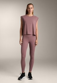 Top cu mâneci scurte, croială lejeră, și colanți cu talie înaltă în nuanță roz-muți. Colanții au o textură netedă, asortați cu pantofi sport negri.