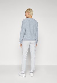 Ljusblå sweatshirt med diamantsmönster, rundad halsringning och ribbade muddar, i kombination med ljusgrå byxor och vita sneakers.