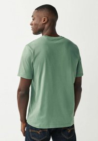 Camiseta de algodón verde menta con cuello redondo, mangas cortas y un corte relajado, combinada con jeans de mezclilla oscura. Textura suave, diseño minimalista.