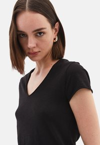 T-shirt nera a maniche corte con scollatura a V, realizzata in tessuto morbido. Caratterizzata da una vestibilità rilassata e un design semplice con linee pulite e dettagli di cucitura sottili.