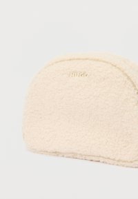 Bolsita semiesférica de color crema, de textura suave, con "HUGO" grabado cerca de la parte superior central, sobre un fondo blanco liso.