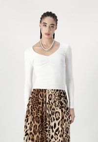 Top bianco a maniche lunghe con scollatura a V e arricciature, abbinato a una gonna stampa leopardata con tonalità di marrone e beige.