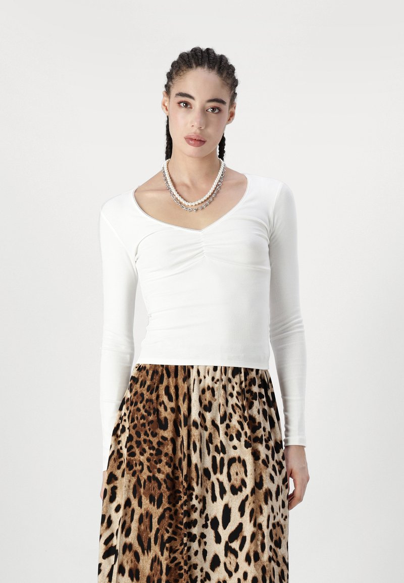 Top bianco a maniche lunghe con scollatura a V e arricciature, abbinato a una gonna stampa leopardata con tonalità di marrone e beige.