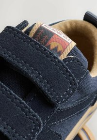 Chaussure velcro bleu marine avec une tige en suède et en tissu. Elle présente une étiquette à motifs avec "Keep Nature Wild" et un intérieur beige.