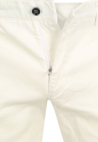Weiße Baumwollhosen mit Reißverschluss, ausgestattet mit einem schwarzen Knopfverschluss und glattem Textil, sichtbare Nähte entlang der Nähte.